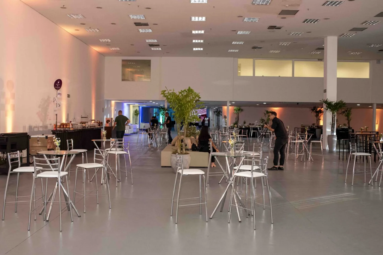 Salão do Expo Boulevard montado para uma celebração, com mesas altas, cadeiras e decoração